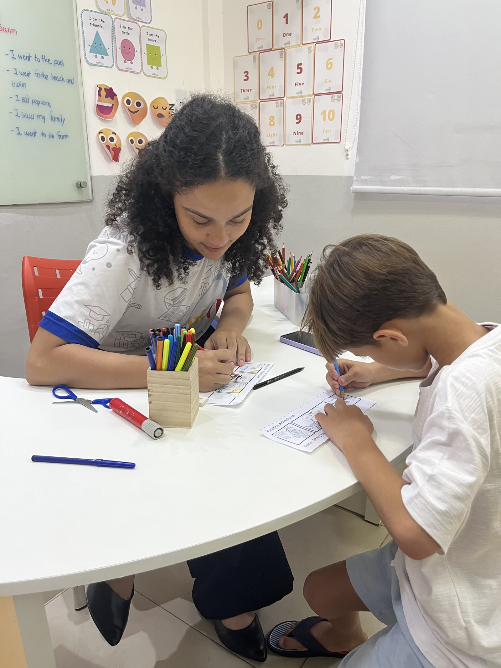 Criança escrevendo palavras em inglês com apoio da professora