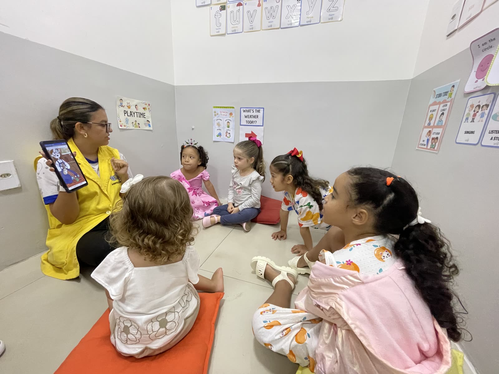 Professora lendo um livro em inglês para crianças sentadas no chão da sala da Eibici